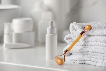 Natural face roller, towels and serum on counter in bathroom. Space for text