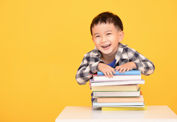  Happy little boy holding large books isolated on yellow background