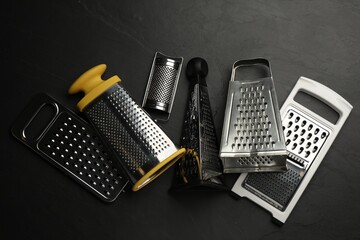 Different modern graters on black table, flat lay