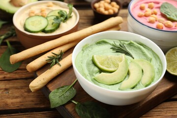 Bowl of delicious green hummus with rosemary, avocado and lime on wooden table