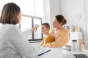 medicine, healthcare and pediatry concept - mother with sick little son and doctor measuring temperature with infrared forehead thermometer at clinic