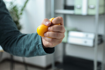 Man squeezing antistress ball in office, closeup