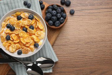 Bowl of tasty crispy corn flakes with milk and blueberries on wooden table, flat lay. Space for text