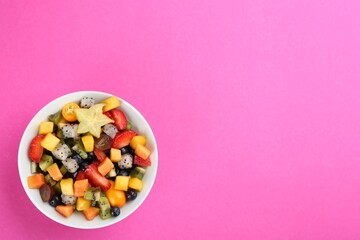 Delicious exotic fruit salad on pink background, top view. Space for text