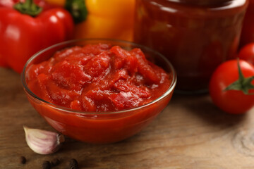 Delicious lecho in glass bowl and fresh ingredients on wooden table, closeup