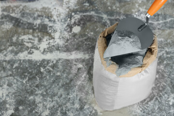 Cement powder and trowel put in bag on stone floor, above view. Space for text