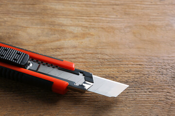 Utility knife on wooden table, closeup. Space for text