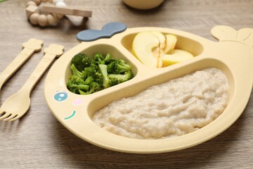 Plastic dishware with healthy baby food on wooden table, closeup