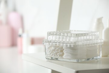 Fototapeta na wymiar Container with cotton swabs and pads on white shelf in bathroom, closeup. Space for text