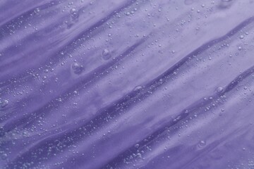 Texture of transparent shower gel on violet background, closeup