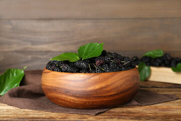 Fresh ripe black mulberries and leaves in bowl on wooden table