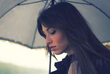 Young woman with umbrella walking in the autumn rain beside river