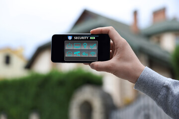 Man using home security application on smartphone in front of house outdoors, closeup