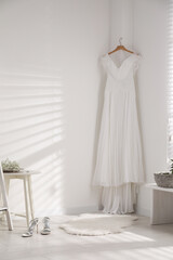 Beautiful wedding dress hanging on white wall in room