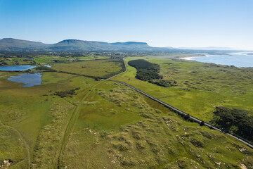 Green country side and Benbulben flat top mountain in county Sligo, Ireland. Warm sunny day. Aerial view. Irish landscape. Blue cloudy sky. Nature scenery.