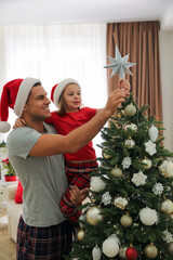 Father and little daughter decorating Christmas tree with star topper indoors