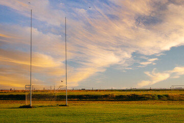 Tall goal posts for Irish National sports in a field of a park at sunrise. Rugby, hurling, camogie and Gaelic football training ground. Nobody. Calm warm color. Dramatic sky.