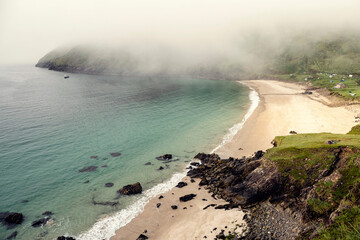Stunning nature scene of Keem bay and beach. Green hills and warm sandy beach. Low clouds over slope of a mountain. Achill island, Ireland. Popular travel area with beautiful nature view.