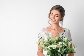 Young bride wearing wedding dress with beautiful bouquet on light background. Space for text