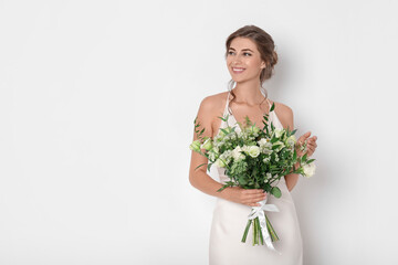 Young bride wearing wedding dress with beautiful bouquet on light background. Space for text