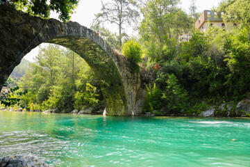 Ancient roman bridge on Dim river in Turkey. Clear turquoise water and green nature.
