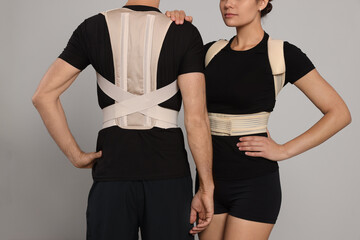 Closeup view of man and woman with orthopedic corsets on grey background - obrazy, fototapety, plakaty