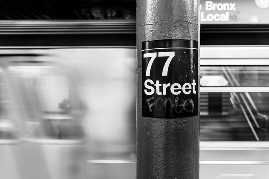 Grayscale shot of a signboard of 77 street on a pipe