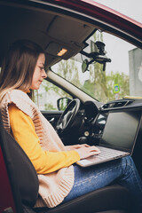 A beautiful girl works on a laptop while sitting in a car, a freelancer or blogger at work, remote...