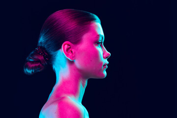Profile view of young fashion model without makeup isolated over dark background in neon light....