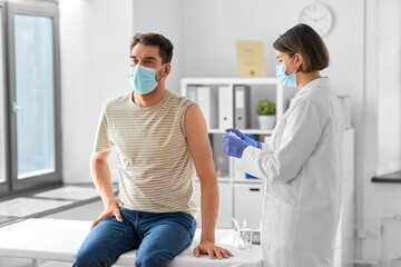 health, medicine and pandemic concept - female doctor or nurse in protective medical mask and gloves disinfecting male patient's skin at hospital