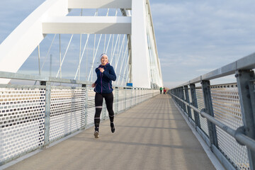 Young smiling woman running on the bridge footpath