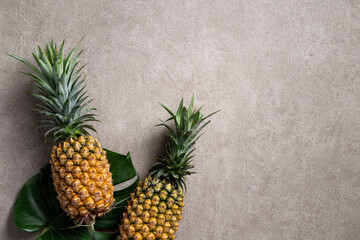 Fresh pineapple with tropical leaves on gray background.