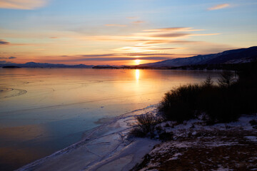 Colorful sunset on the frozen lake Baikal. Clean ice with cracks. Winter landscape