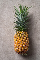 Fresh pineapple with tropical leaves on gray background.