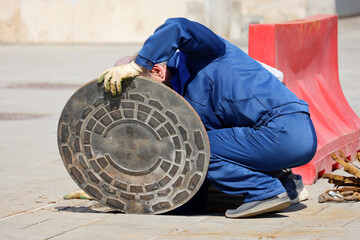 Workers in blue uniform over the open sewer hatch on a street. Concept of repair of sewage,...