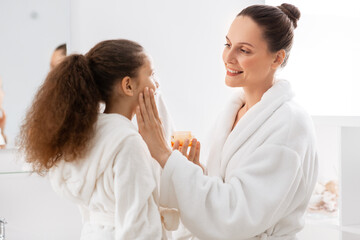 beauty, hygiene, morning and people concept - happy smiling mother and daughter with moisturizer at bathroom