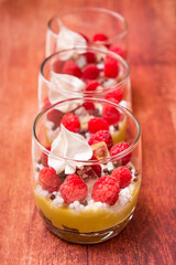 Three verrines with pistachio cream, raspberries and white meringue on brown background