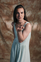 Fototapeta na wymiar Brunette nonbinary person in dress blowing air kiss at camera on abstract brown background.