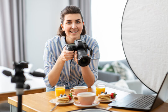 blogging, profession and people concept - happy smiling female food photographer with camera photographing pancakes, coffee and orange juice in kitchen at home