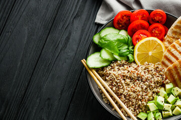 quinoa salad with grilled chicken and vegetables on a black wooden rustic background