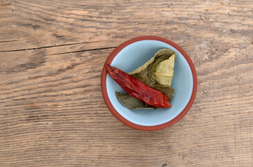 Kaffir lime leaves and a red chili pepper in a small bowl on a wood background.