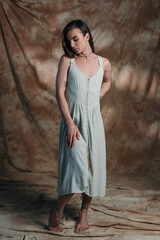 Barefoot queer person in sundress standing on abstract brown background.