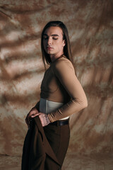 Young nonbinary person holding jacket on abstract brown background.