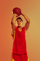 Portrait of young man, concentrated basketball player throwing ball into basket isolated over...