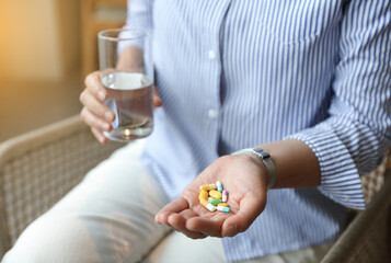 woman holding a glass of water and taking vitamins and pills on a light background. close up.