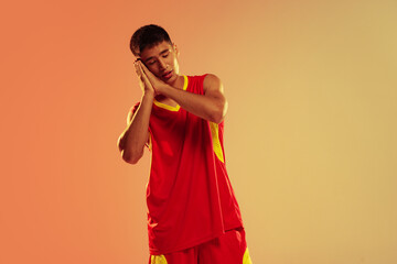 Portrait of young man, basketball player looking sleepy and tired isolated over orange studio background in neon light