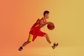 Fototapeta na wymiar Dynamic portrait of young man, basketball player in motion, dribbling isolated over orange studio background in neon light