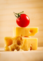 Red tomato placed on pieces of Swiss cheese. Beautiful food photo of Swiss cheese and cherry tomato.