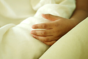 Close up of a child's hand in a soft bed. A peacefully sleeping kid's hand resting on the bed.