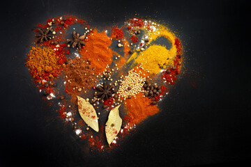 Multiple various spices forming a heart shape, isolated on black